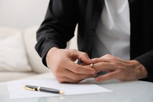 Picture of a man taking off his wedding ring as he's signing divorce papers.