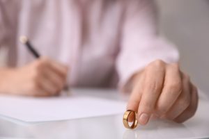 Picture of a woman holding her wedding ring as she's signing papers in the background.
