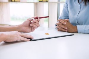 Picture of a man handing a pen to a woman with papers and two wedding rings sitting on the table between them.