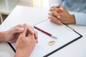 Picture of a man and a woman with a clipboard, papers, a pen, and wedding rings on the table between them.