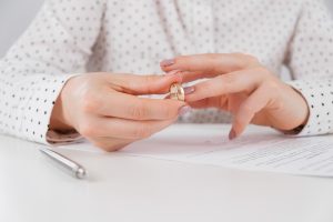 Picture of a woman taking off her wedding ring with a paper and a pen on the table in front of her.