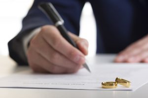 Picture of a man signing paperwork with two gold rings on the top left corner.