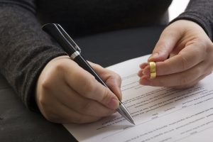 Picture of a man holding a gold ring as he signs paperwork.