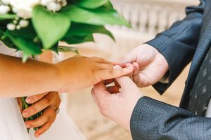 Picture of a groom placing a ring onto a bride's finger.