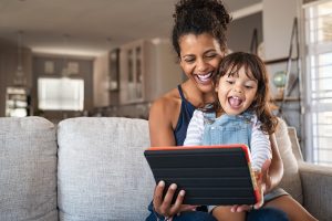 Picture of a child sitting on a woman's lap, looking at a tablet with her.