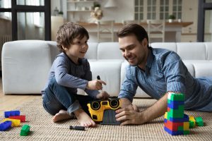 Picture of a man and a child playing with toys on the floor.