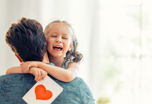Picture of a father hugging his daughter as she holds a card with a heart on the front.