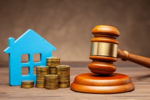 Picture of a miniature house figurine, stacks of coins, and a gavel.