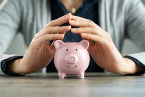 Picture of a person holding their hands together above a piggy bank.