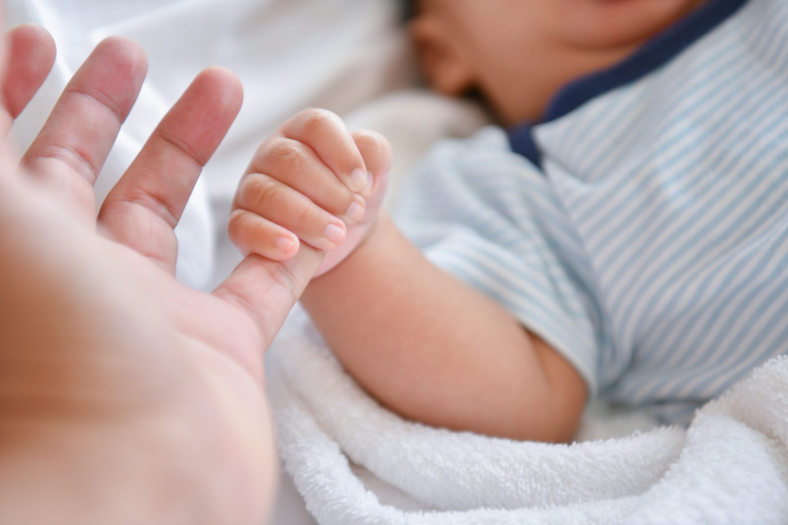 Picture of a baby holding onto an adult's pinky finger.