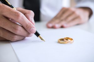 Picture of a man signing divorce papers, with two gold wedding rings sitting on top of the papers.