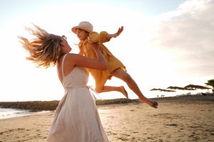 Picture of a mother lifting her daughter in the air on a beach.
