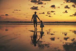 Picture of a father and daughter walking on a beach at sunset.