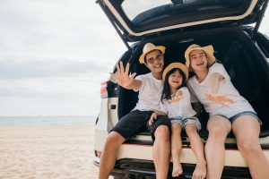 Picture of a happy family sitting in the hatchback of a vehicle parked on a beach.