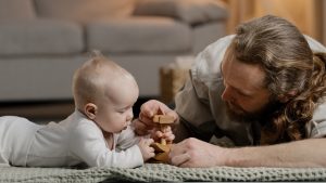 Picture of a father and his infant son playing with blocks on their living room rug.