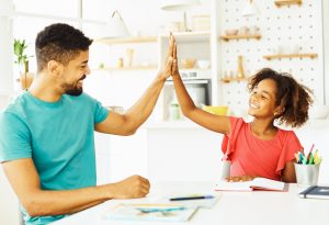 Picture of a father high-fiving his daughter as he helps her with homework.