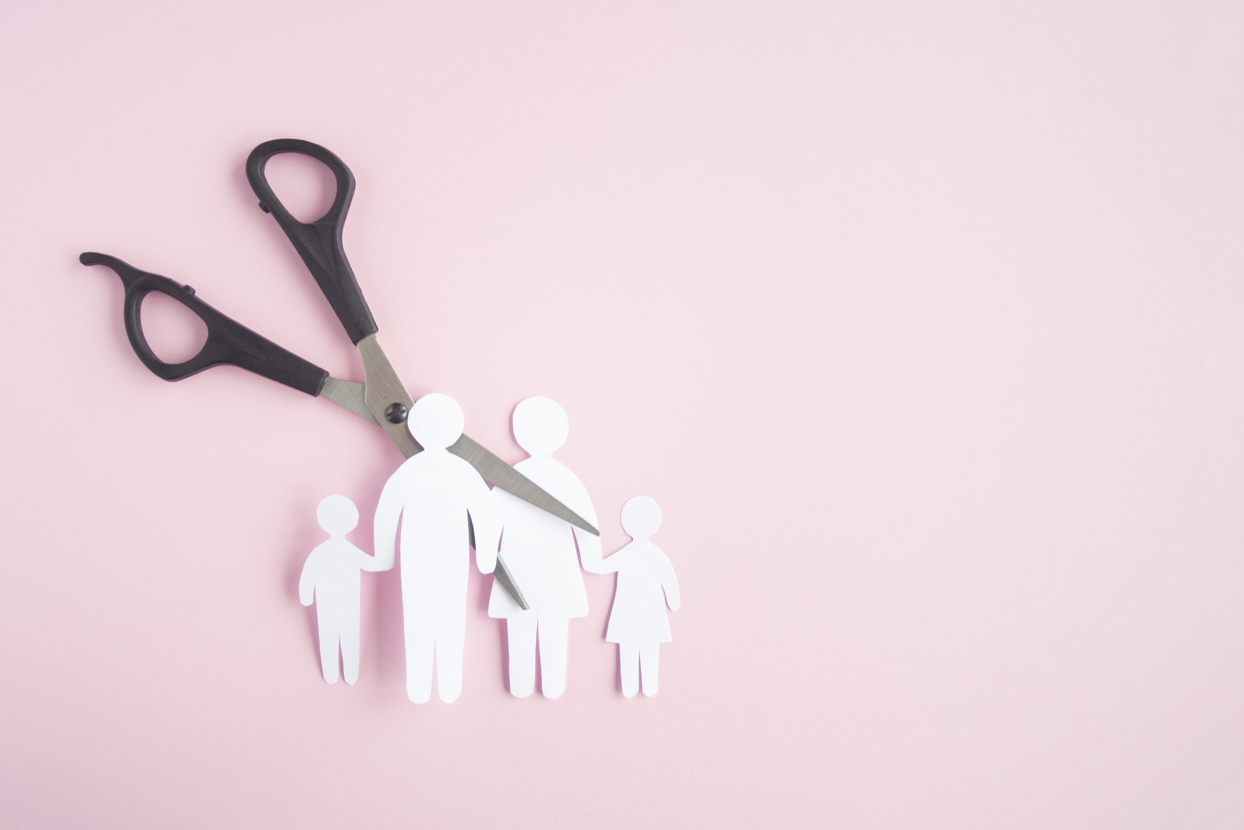 Picture of a pair of scissors cutting a paper cutout of a family in half.