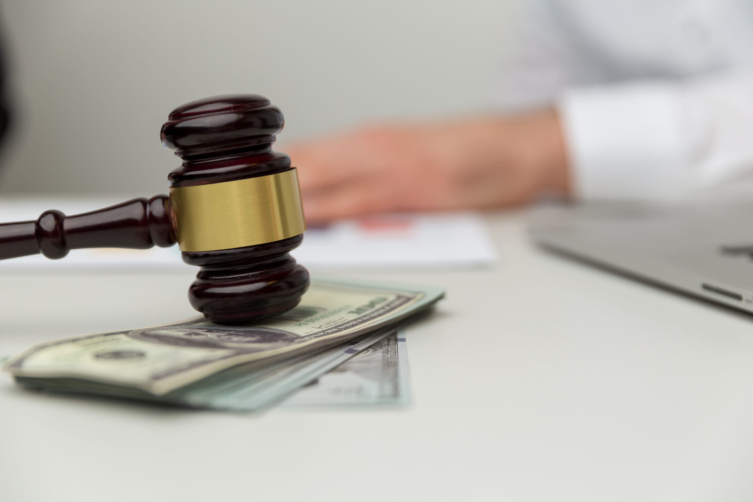 Picture of a gavel on top of a stack of money, with a divorce attorney sitting in the background.