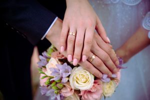 Picture of a bride and groom showing their wedding rings and holding the bridal bouquet.